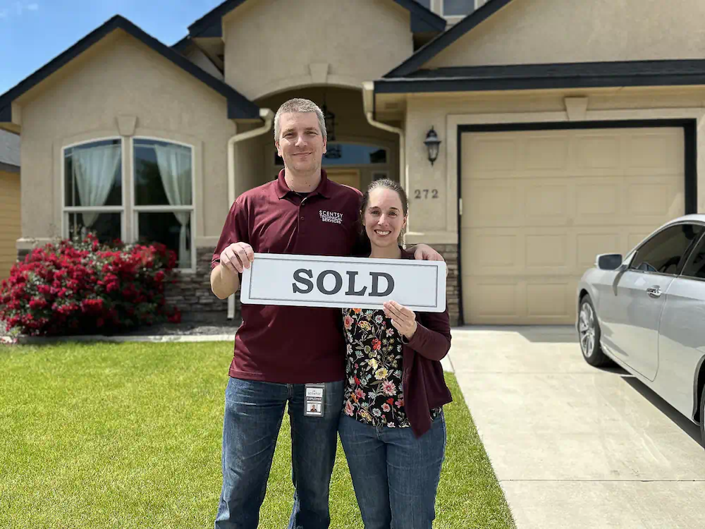 Happy buyers holding a sold sign in their front yard outside of a beautifully maintained Meridian home with a custom patio.