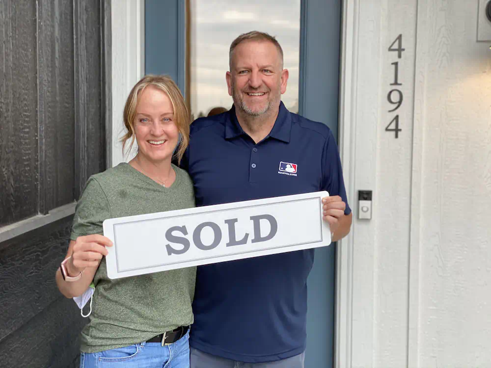 Happy relocating couple standing in front of their luxury new construction townhome next to Spurwing Golf Course.