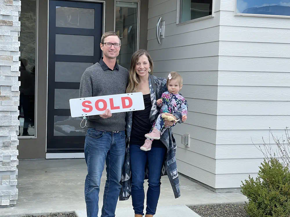 Adorable family holding a sold sign, and their first baby, who bought a modern Southeast Boise home.