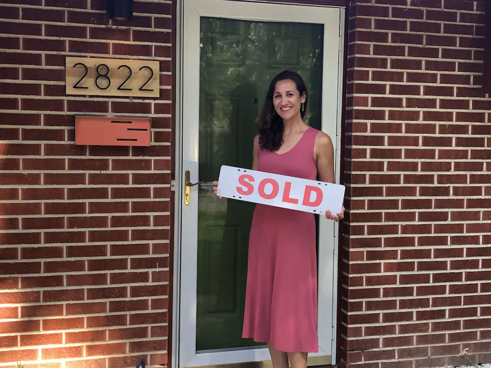 Happy buyer with a sold sign standing in front of her classic mid-century ranch on the Boise Bench.